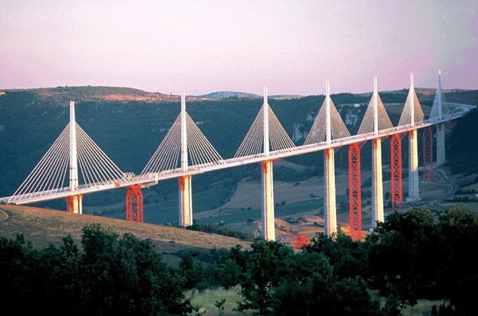 پل میلو

پل میلو بلندترین پل جاده‌ای جهان به ارتفاع ۳۴۳ متر است که در بالای رودخانه تارن در جنوب فرانسه قرار دارد. این پل توسط میشل ویرلوژو (مهندس سازه) و نورمن فاستر (معمار) طراحی و در دسامبر سال ۲۰۰۴ توسط ژاک شیراک رئیس جمهور سابق فرانسه افتتاح شد.

جاده پل به طول ۲۴۶۰ متر از مقاطع فولادی در ۸ دهنه با عرض ۳۲ متر و فاصله متوسط ۳۴۲ متر بین هر ستون تشکیل شده است. این جاده بیش از ۳۶،۰۰۰ تن وزن داشته و با عمق ۴٫۲ متر به عنوان طولانی‌ترین جاده کابلی پل در جهان به حساب می‌آید. جاده پل شیبی ۳٪ از جنوب به شمال طی کرده و همچنین انحنایی به شعاع ۲۰ کیلومتر در سطح را به دلیل ایجاد زاویه دید بهتر برای رانندگان داراست.

جاده پل بر روی ۷ ستون بتنی که ارتفاع آن‌ها از ۷۷ تا ۲۴۶ متر متغیر است قرار گرفته است. ضخامت ستون‌ها در پی ۲۴٫۵ متر بوده که در نهایت به ۱۱ متر ختم می‌شود. هر کدام از ستون‌ها نگهدارنده دکلی ۸۷ متری است که ۷۰۰ تن وزن دارد.