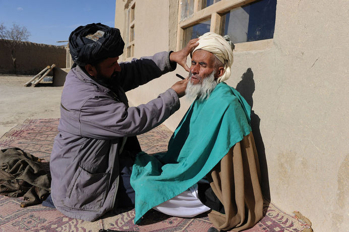 آرایشگر روستایی در حال زدن ریش مردی در ولایت غزنی افغانستان در سال ۲۰۱۱